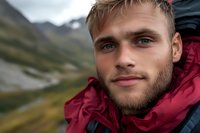 Young Caucasian male hiker with beard wearing red jacket in mountain landscape. Outdoor adventure portrait with dramatic sky and valley background for travel content.