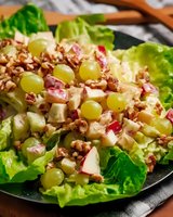Fresh waldorf salad with green grapes, apples, celery, and walnuts served on lettuce leaves, dressed in creamy mayonnaise dressing on dark plate.