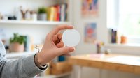 Hand holding blank white circle disc in modern home office workspace with shelves and natural light.