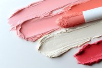Creamy textured makeup foundation and concealer swatches in coral, beige and red shades smeared on white background showing product consistency and color range.