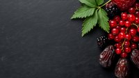 Fresh red currants and ripe blackberries with green leaves arranged with dried dates on dark slate stone background, corner food composition for menu design.