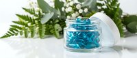 Blue skincare gel in glass jar with natural fern and eucalyptus leaves on white marble surface for beauty and wellness cosmetic products.