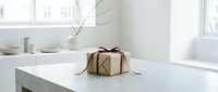 Kraft paper wrapped gift box with brown ribbon bow on marble table in minimalist white interior, holiday present concept.