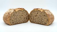 Freshly baked multigrain bread loaf cut in half showing dense texture with seeds and grains, artisan bakery product for healthy eating concepts.