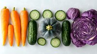 Fresh organic vegetables arranged in neat rows on white background - carrots, sliced cucumber, pumpkin and purple cabbage creating minimalist food composition.