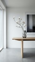 Minimalist Scandinavian interior with magnolia branch in smoked glass vase on oak table, white walls, concrete floor, natural light.