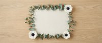 Flat lay blank card framed with eucalyptus branches and white anemone flowers on wooden background, copy space for text.