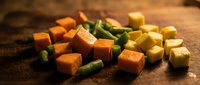 Colorful diced vegetables including orange carrots, green beans and yellow potatoes arranged on rustic wooden cutting board for healthy cooking preparation.