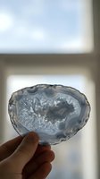 Hand holding translucent agate geode slice with crystalline formations against bright window light showcasing natural mineral patterns and textures.