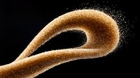 Flowing golden sand particles forming elegant curved shape against black background, dynamic motion captured in freeze frame with scattered dust particles.