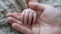 Tiny newborn hand resting in a parent's open palm on a soft knit blanket, symbolizing love, care, and new life.