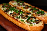 Fresh baked garlic bread topped with melted mozzarella cheese, sauteed mushrooms and chopped parsley on wooden cutting board, close up view of appetizer.