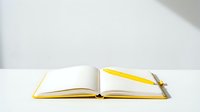 Open notebook with blank pages and yellow metal pen on white surface with soft shadow lighting.