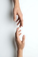 Two hands reaching toward each other against white background symbolizing connection, help, support, teamwork, partnership and human interaction.