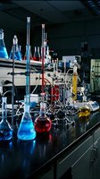 Chemistry laboratory with colorful chemical solutions in glass flasks and beakers on black lab bench for scientific research and experimentation.