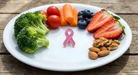 Healthy colorful foods arranged around pink ribbon symbol on white plate representing cancer awareness nutrition and wellness support.
