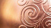 Elegant copper metallic surface with ornate swirl patterns and warm golden lighting effects for luxury design projects and decorative backgrounds.