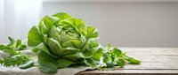 Fresh green lettuce head with leafy herbs on rustic wooden table surface for healthy cooking and organic food preparation concepts.