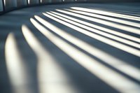 Dramatic diagonal light and shadow pattern on white wall from window blinds creates abstract geometric shapes in modern minimalist interior space.