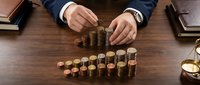 Businessman in suit stacking golden coins on wooden desk representing financial growth, investment planning and wealth management strategies.
