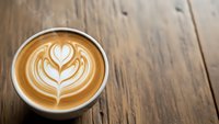 Latte art heart pattern in coffee cup on rustic wooden table background for cafe menu design and beverage marketing materials.