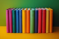 Row of colorful hardcover books standing upright against green gradient background on yellow surface, spines showing vibrant rainbow spectrum arrangement.