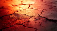 Dramatic cracked dry soil texture illuminated by warm red sunset light creating abstract pattern of deep fissures and natural erosion lines. Suitable for environmental themes.