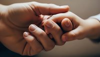 Adult hands gently holding baby feet in tender moment showing parental love and care for newborn child in soft warm lighting.