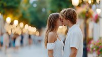 Young couple sharing romantic kiss on charming European street with warm evening lights and colorful flowers creating intimate atmosphere for love stories.