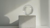 Clear glass sphere on minimalist concrete pedestal casting soft shadows against white wall, modern artistic composition with clean lines and geometric shapes.