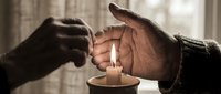 Hands of two people shielding a lit candle flame together, symbolizing hope, unity, and support during difficult times or charitable giving.