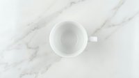 Empty white ceramic mug on marble surface, overhead view, isolated on white background, ready for mockup designs, branding, and product presentations.