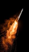 Powerful rocket launch with bright orange flames and sparks against black night sky. Space exploration mission takeoff with dramatic fire trail and smoke.