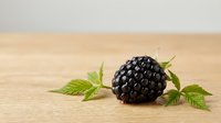 Fresh blackberry with green leaves on wooden surface, suitable for food photography, culinary blogs, and healthy eating content.