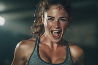 Young athletic woman with freckles shouting in triumph during intense workout, expressing raw emotion and determination in dark gym environment.