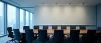 Modern corporate boardroom with long wooden conference table and black executive chairs overlooking city skyline through floor-to-ceiling windows.