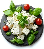 Fresh feta cheese cubes with cherry tomatoes and basil leaves on round slate board, Mediterranean appetizer for gourmet cuisine.