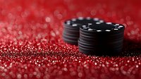 Black poker chips stacked on sparkling red glitter surface with bokeh effect background, creating luxurious casino atmosphere for gaming and entertainment concepts.