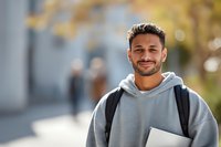 Young male student with backpack smiling at camera on college campus with autumn background and soft bokeh effect.
