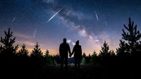 Silhouetted couple holding hands gazing at starry night sky with meteor shower and milky way galaxy above forest landscape. Romantic astronomy scene for travel, nature, and celestial themes.