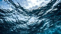 Underwater view of ocean waves creating dynamic patterns with sunlight filtering through deep blue water surface from below.
