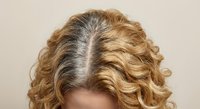 Young Caucasian woman with curly blonde hair showing gray roots, hair care and coloring concept for beauty salon services.