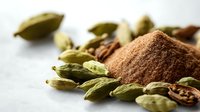 Ground cardamom powder and whole green cardamom pods scattered on light surface, aromatic spices macro photography for culinary and cooking concepts.