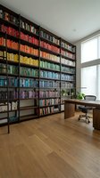 Modern home office with floor-to-ceiling bookshelf organized by color spectrum, wooden desk, ergonomic chair and natural light for productivity workspace design.