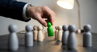 Business hand selecting green wooden figure from crowd representing talent recruitment, leadership choice, and human resources management in corporate environment.