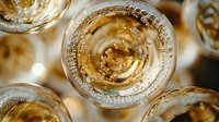 Overhead view of sparkling champagne glasses with golden bubbles rising in crystal flutes, creating elegant circular patterns against light background.