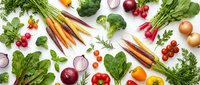 Fresh organic vegetables and herbs scattered on white background including colorful carrots, broccoli, radishes, onions, peppers and leafy greens for healthy cooking.