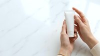 Woman holding blank white cosmetic tube on marble background for skincare product branding and packaging mockup design.