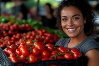 Young African American woman with curly hair smiling while holding fresh vine tomatoes at farmers market. Natural lighting highlights fresh produce and genuine expression.