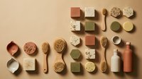 Flat lay arrangement of natural skincare and wellness products including handmade soaps, brushes, and cosmetic bottles on neutral beige background for beauty and spa marketing.